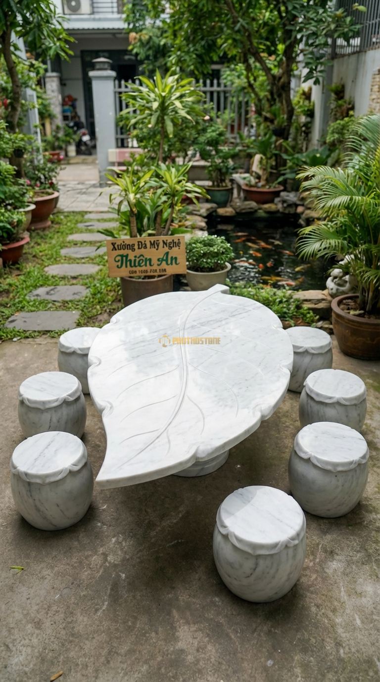 Bộ Bàn Ghế đá Nguyên Khối Dáng Lá, Chất Liệu đá Trắng Yên Bái, Kiểu Dáng phiến đá Mỏng, Bè Rộng, Uốn Lượn Tự Nhiên Như Chiếc Lá Sen Khổng Lồ. Bàn: 160 x 120 x 55 Cm Đôn: Tròn Thấp 30 x 30 Cm (6 Đôn)